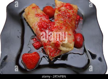 Eingerollte Pfannkuchen gefüllt mit Hüttenkäse und Erdbeermarmelade mit Beeren Stockfoto
