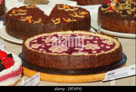 Konditorstand mit Variationen von nicht gebackenen ROHEN Kuchen, Aronia oder auch Apfelbeerkuchen mit Mandelnüssen im Vordergrund, Nahaufnahme ohne Leute bei farme Stockfoto