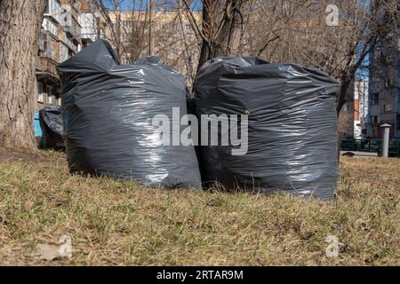 Zwei schwarze Säcke mit Müll, alte gefallene Blätter, Äste auf dem Boden. Frühjahrsputz. Straßenreinigung in der Stadt. Stockfoto