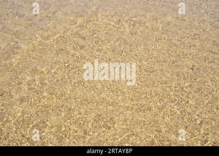 Blick von oben auf das transparente, saubere Wasser des Meeres. Gelber Sand durch Wasser gesehen. Sonnenstrahlen reflektieren auf Wellen. Sommer, Ferien, Meereslandschaft, Urlaub, Stockfoto