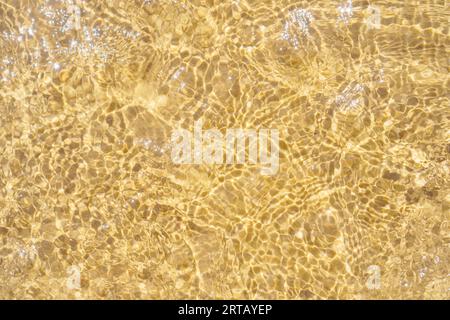 Blick von oben auf das transparente, saubere Wasser des Meeres. Gelber Sand durch Wasser gesehen. Sonnenstrahlen reflektieren auf Wellen. Sommer, Ferien, Meereslandschaft, Urlaub, Stockfoto