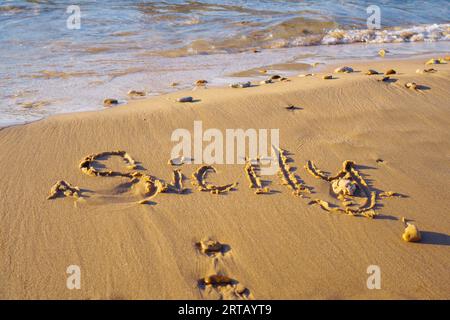 Nahaufnahme des Inschriftenwortes Sizilien, das auf nassem Sand der Strandküste nach Gezeiten in der Nähe von Meereswellen bei Sonnenuntergang geschrieben wurde. Sommer, Urlaub, Urlaub Stockfoto