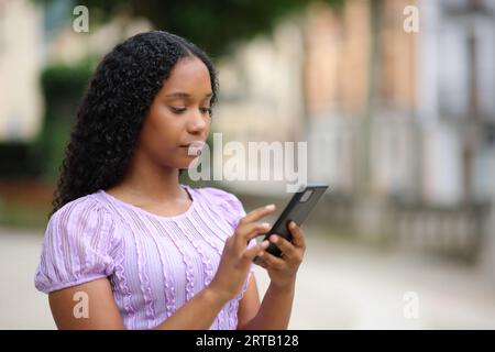 Schwarze Frau, die Handy benutzt, geht auf der Straße spazieren Stockfoto