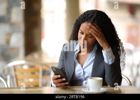 Besorgte schwarze Geschäftsfrau, die schlechte Nachrichten am Telefon auf einer Bar-Terrasse abfragte Stockfoto