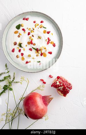 Joghurt mit Rosinen, Pistazien und Granatapfelkernen in Teller auf grünem Hintergrund. Draufsicht. Gesundes Frühstück, gesundes Esskonzept Stockfoto