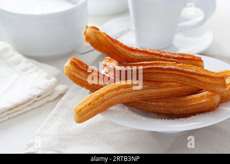 Mehrere Churros auf einem kleinen Teller auf einem Tisch zum Frühstück. Stockfoto