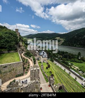 Schloss Reichenstein: Blick auf die Vorburg, das Turniergelände und das Schlosshotel, im Hintergrund der Königstein-Wachturm und der Rhein V. Stockfoto