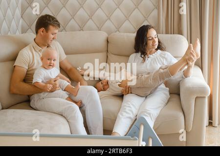 Familie mit zwei Kindern auf der Couch, die Spaß hat. Mather, Vater, Baby und Kleinkinder freuen sich am Morgen im Wohnzimmer. Kinder, die mit Paren spielen Stockfoto