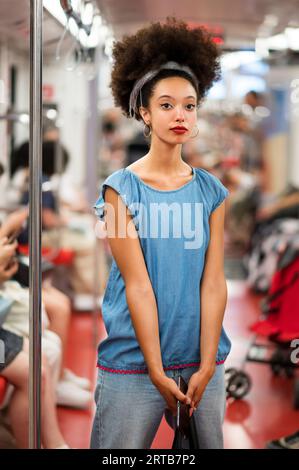 Stilvolle junge gemischte Rasse weibliche Millennials mit dunklen Afro-Haaren und roten Lippen in lässigem Outfit, die Kamera beim Stehen in der U-Bahn mit sma Stockfoto