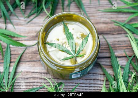 Aus Samen hergestellter Urbech wurde in einem Glasgefäß auf einer Schicht mit Marihuanablättern ausgegraben. Köstliche süße grüne Pasta Delikatesse aus Hanf. Stockfoto