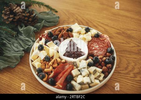 Moderne Käseplatte mit verschiedenen Käsesorten, Salami und Prosciutto, Nüssen und Preiselbeersauce als weihnachtsbaum auf festlichem Tisch. Käsevorspeisen, c Stockfoto