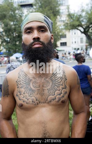 Zuschauer am Eastern Parkway bei der jährlichen West Indian Caribbean Parade am Labor Day in Brooklyn, New York. Mann mit einem Tattoo, das Frieden und Einheit repräsentiert. Stockfoto