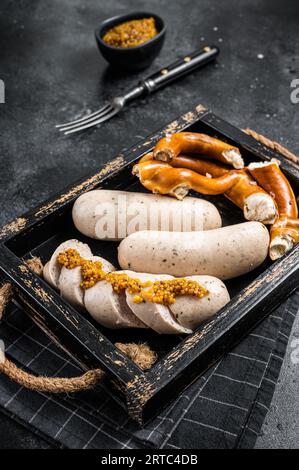 Bayerisches Gericht mit weißen Würstchen und süßem Senf in einem Holztablett mit Brezel. Schwarzer Hintergrund. Draufsicht. Stockfoto