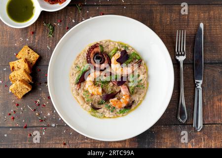 Risotto mit Jumbogarnelen und Oktopus auf weißem Porzellanteller auf Holztisch. Meeresfrüchte-Risotto Stockfoto