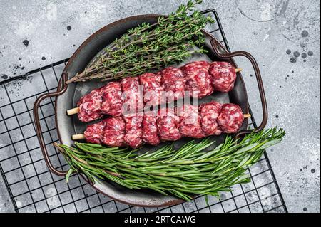 Roher türkischer Urfa-Kebab mit Kräutern, Gewürzen und Fleischgabel. Grauer Hintergrund. Draufsicht. Stockfoto