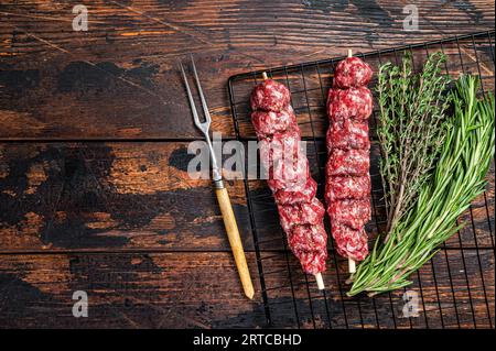 Roher Kofta, Kofte-Dönerspieße mit Rindfleisch- und Lammfleisch und Gewürzen zum Kochen. Hölzerner Hintergrund. Draufsicht. Leerzeichen kopieren Stockfoto