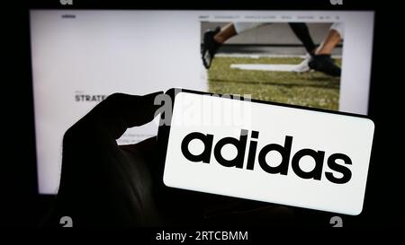 Person, die ein Smartphone mit dem Logo des deutschen Bekleidungs- und Schuhherstellers Adidas AG auf dem Bildschirm vor der Website hält. Konzentrieren Sie sich auf das Display des Telefons. Stockfoto