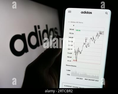 Person, die ein Mobiltelefon mit Webseite des deutschen Bekleidungs- und Schuhherstellers Adidas AG auf dem Bildschirm mit Logo hält. Konzentrieren Sie sich auf die Mitte der Telefonanzeige. Stockfoto