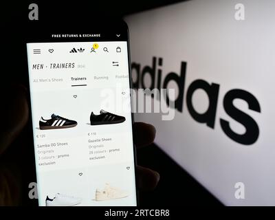 Person, die ein Mobiltelefon mit Webseite des deutschen Bekleidungs- und Schuhherstellers Adidas AG auf dem Bildschirm mit Logo hält. Konzentrieren Sie sich auf die Mitte der Telefonanzeige. Stockfoto