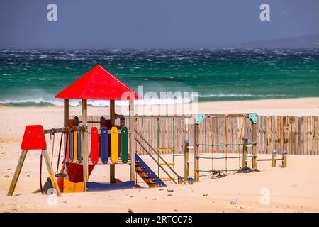 Ein farbenfroher Spielplatz am stürmischen Sandstrand von Conil de la Frontera an der andalusischen Costa de la Luz, Spanien Stockfoto