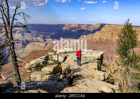 Eine Frau am Rand des Grand Canyon erhebt ihre Arme und blickt auf den Grand Canyon, Arizona, USA Stockfoto