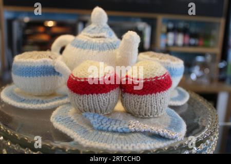 Handgestrickte Teekanne, Tassen und zwei Kuchen Stockfoto