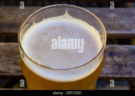 Gekühltes Glas Bier auf dem Holztisch. Unscharfes Straßencafé im Sommer draußen im Hintergrund Stockfoto