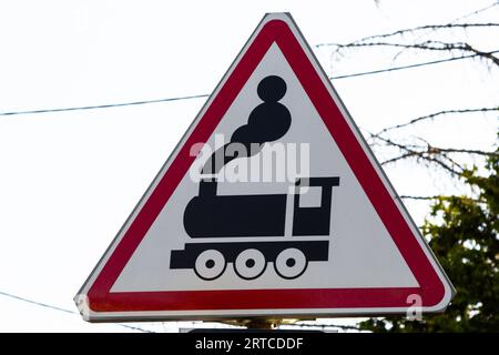 Rot-weißes Schild für die Eisenbahnstraße, Schild für die Bahnüberquerung, im Hintergrund fährt ein Auto über die Schienen. Stockfoto