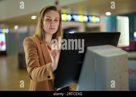 Frau überprüft ihren Flug am Selbstbedienungsterminal am Flughafen. Stockfoto