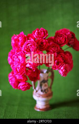 Blumenstrauß aus rosa Rosen in einer Keramikvase auf grünem Hintergrund. Stockfoto