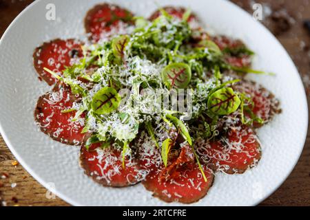 Rindfleisch-Carpaccio. Borettane-Zwiebeln, sonnengetrocknete Tomaten, Trüffeldressing, Rucola-Salat, Parmesankäse. Traditionelle italienische Antipasti-Snacks serviert Stockfoto