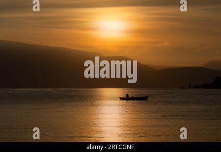Sonnenaufgang mit Fischer mit Boot und Reflexion der Sonne, Salò, Provinz Brescia, Italien Stockfoto