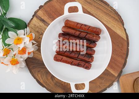 Blick von oben auf gebratene und gegrillte Würstchen mit Sauce auf einem weißen Teller und isoliertem Hintergrund. Würzige Hähnchenwürste in Öl gebraten. Stockfoto