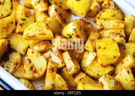 Rohe Kartoffelscheiben in Gewürzen, die gebacken oder geröstet werden können. Frische Kartoffelspalten, gemischt mit Kräutern und Gewürzen auf rustikale Weise. Rohe Kartoffeln mit Gewürzen Stockfoto