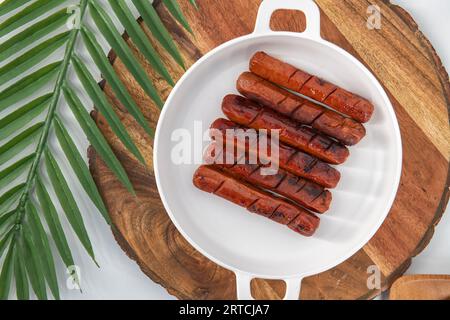 Blick von oben auf gebratene und gegrillte Würstchen mit Sauce auf einem weißen Teller und isoliertem Hintergrund. Würzige Hähnchenwürste in Öl gebraten. Stockfoto