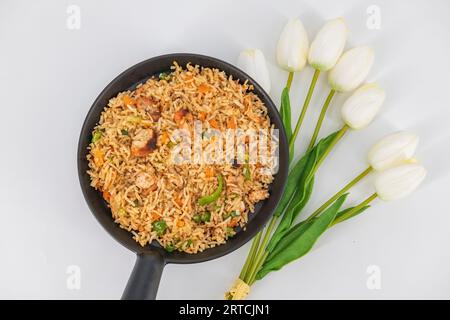 Hühnchen gebratener Reis in schwarzer Servierschüssel isoliert auf weißem Hintergrund. Szechuan Rice ist ein indochinesisches Gericht mit Paprika, grünen Bohnen und Karotten Stockfoto