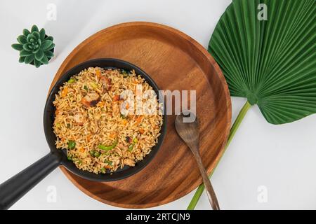 Hühnchen gebratener Reis in schwarzer Servierschüssel isoliert auf weißem Hintergrund. Szechuan Rice ist ein indochinesisches Gericht mit Paprika, grünen Bohnen und Karotten. Stockfoto