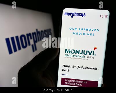 Person, die ein Mobiltelefon mit Webseite des deutschen biopharmazeutischen Unternehmens MorphoSys AG auf dem Bildschirm mit Logo hält. Konzentrieren Sie sich auf die Mitte der Telefonanzeige. Stockfoto