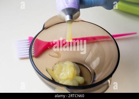 Mädchen in blauen Gummischutzhandschuhen, die eine Bürste in den Händen halten und umrührende Haarfärbung Nahaufnahme Colorist Haarpflege zu Hause Haarmaske. Stockfoto