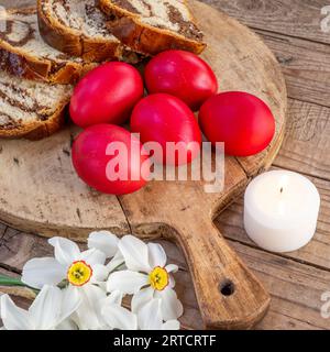 Traditionelles rumänisches ostergericht Cozonac oder Süßbrot auf Holztisch und farbige ostereier und weiße Narzissenblüten Stockfoto