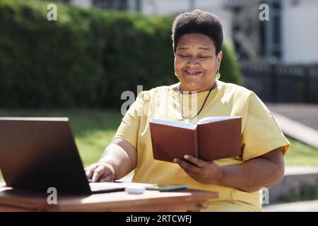 Porträt der lächelnden Schwarzen Seniorfrau, die im Sonnenlicht draußen Buch liest Stockfoto