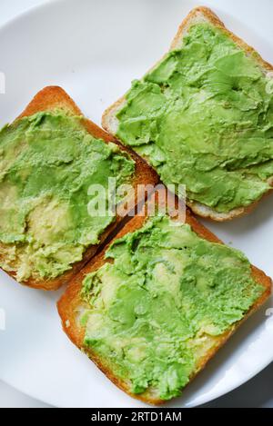 Avocado-Pasta auf gebratenem Toast. Gemüse auf Brot verteilt. Veganes Frühstück auf einem weißen Teller. Stockfoto