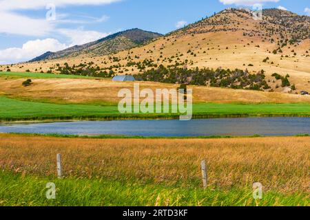 Farmland und See entlang der Montana Road 359 südlich von Butte, Montana, mit den Hügeln des Beaverhead-Deerlodge National Forest als Hintergrund. Stockfoto