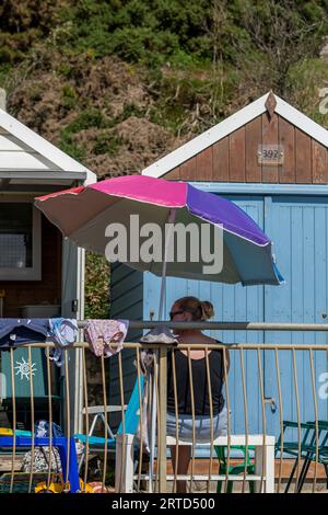 Junge Frau, die vor einer Strandhütte unter einem Sonnenschirm oder Sonnenschirm am Strand in bournemouth uk sitzt Stockfoto