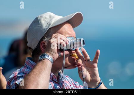 Mann mittleren Alters, der eine Baseballmütze mit einer kleinen Digitalkamera trägt, um ein Foto zu machen. Stockfoto