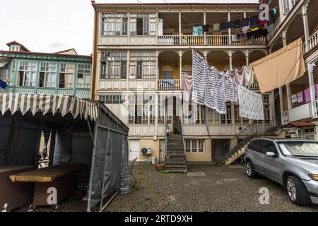Ein typischer Innenhof in Tiflis Altstadt: Ein mehrstöckiges Wohngebäude mit charakteristischen Shushabandi-Holzbalkonen – die verglasten Holzstrukturen aus dem 19. Jahrhundert, die typisch für Tiflis sind – und Waschen auf Linien über den gepflasterten Innenhof. Der Begriff „Shushabandi“ leitet sich vom persischen Wort für Glas (Shisha) ab; die Balkone wurden ursprünglich entworfen, um den Bewohnern mehr Wohnraum zu bieten. Betlemi Street, Kala, Ortachala, Bezirk Krtsanisi, Tiflis, 0108, Georgien Stockfoto