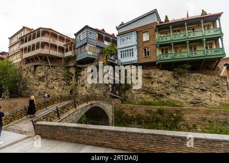 Die Menschen laufen über eine Brücke und eine Wendeltreppe in Abanotubani, Tiflis, Georgien. Die Brücke ist mit Liebesschlössern bedeckt. Traditionelle Häuser mit Balkonen stehen auf einer Felswände Stockfoto