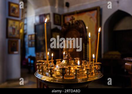 Messingkerzenhalter mit brennenden Wachskerzen in der Metekhi-Kirche in Tiflis. Das Anzünden von Votivkerzen ist ein zentrales Element des Gottesdienstes in der georgisch-orthodoxen Kirche; Ikonen und die Ikonostase der mittelalterlichen Kirche sind im Hintergrund zu sehen. Aufstieg nach Metekhi, Zemo Avlabari, Metromsheni, Bezirk Isani, Tiflis, 0144, Georgien Stockfoto