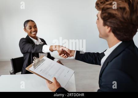 Glückliche Personalleiterin und schwarze Bewerberin, die nach erfolgreichem Arbeitsgespräch im Amt die Hand schüttelt Stockfoto