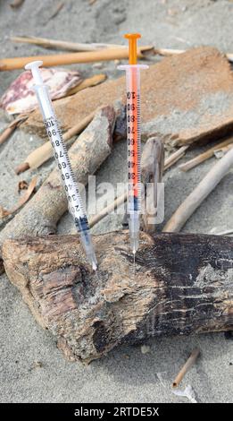 Zwei gebrauchte Einweg-Spritzen, die am Sandstrand aufgegeben wurden Stockfoto